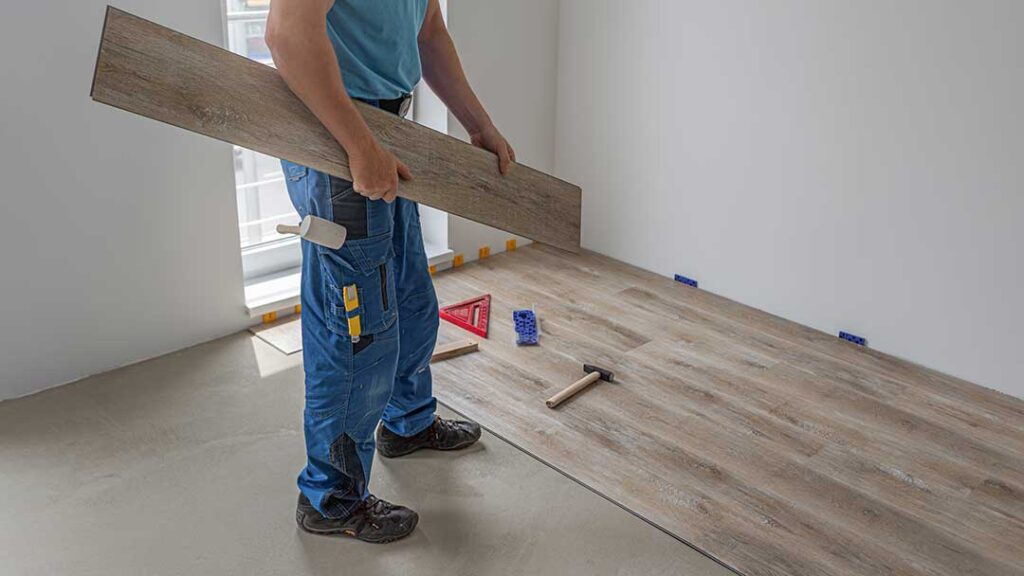 A person unrolling underlayment over a wooden floor before installing new flooring above.