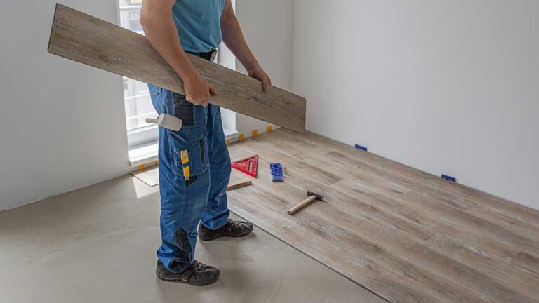 A person unrolling underlayment over a wooden floor before installing new flooring above.