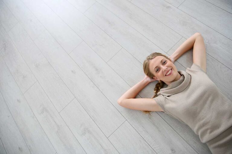 A person gently placing felt pads under the legs of a wooden chair on a hardwood floor.