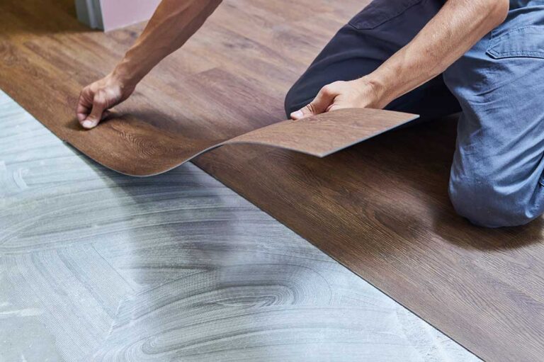 Person measuring a clean subfloor beside stacked flooring planks and installation tools.